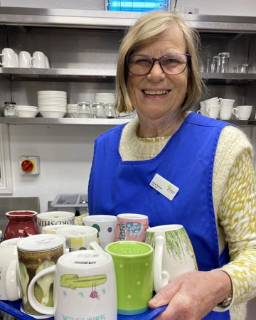 Woman carries tray of mugs in hospice kitchen 