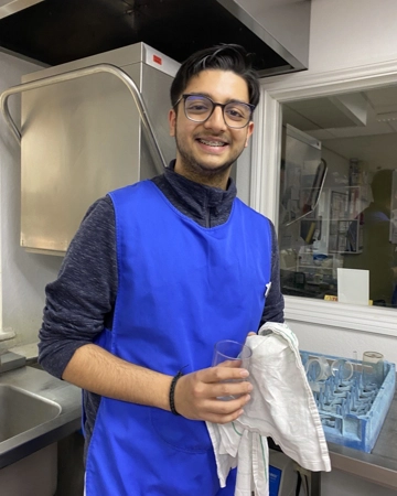 Teenage volunteer dries glass in hospice kitchen